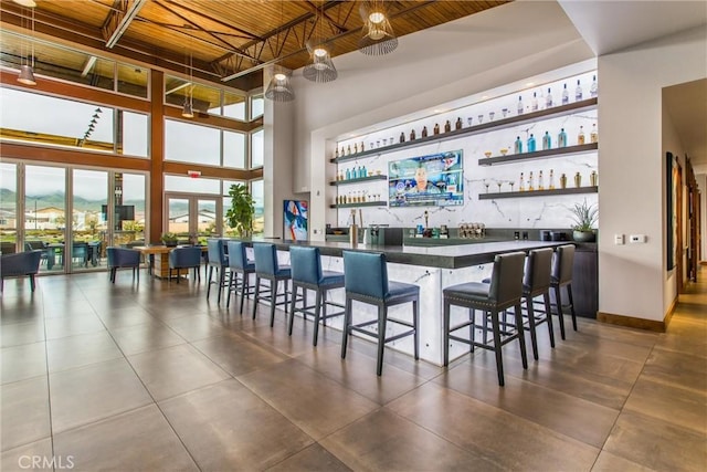 bar with wet bar, a towering ceiling, wooden ceiling, tile patterned floors, and baseboards