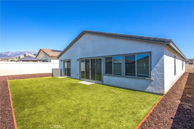 rear view of house featuring a tiled roof, a fenced backyard, stucco siding, a lawn, and a mountain view