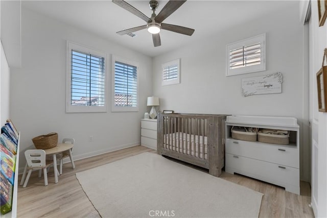 bedroom with a crib, baseboards, wood finished floors, and a ceiling fan
