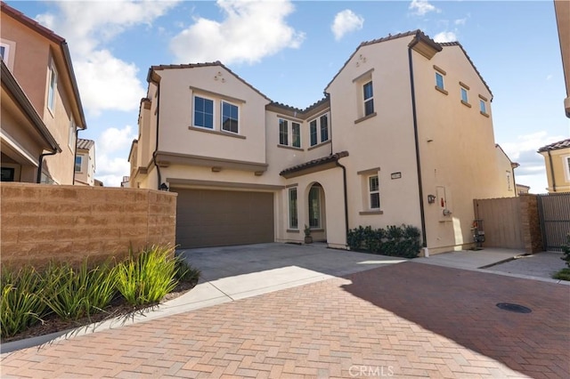 mediterranean / spanish home with a garage, a tiled roof, decorative driveway, and fence
