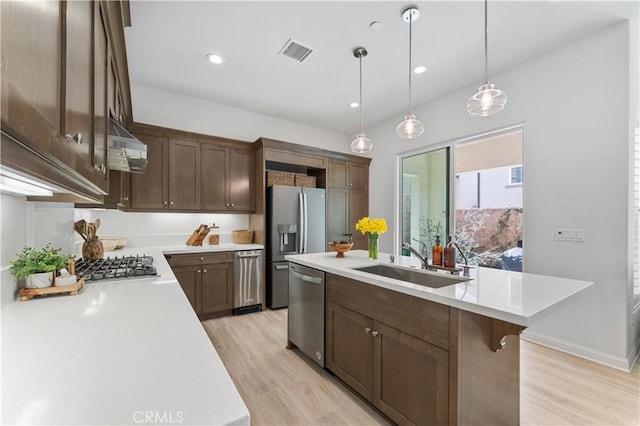 kitchen featuring a sink, stainless steel appliances, light wood finished floors, range hood, and visible vents