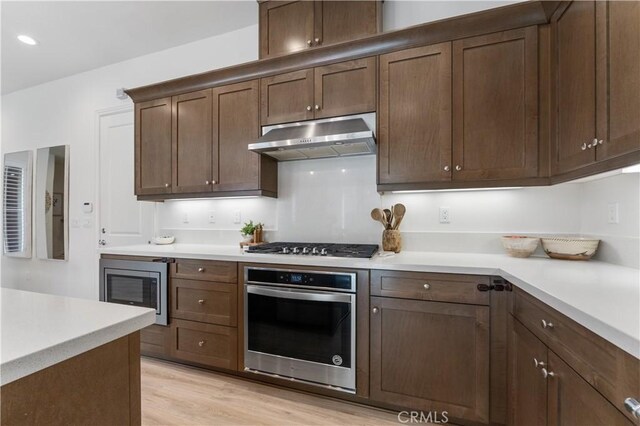 kitchen featuring recessed lighting, under cabinet range hood, stainless steel appliances, light countertops, and light wood-type flooring