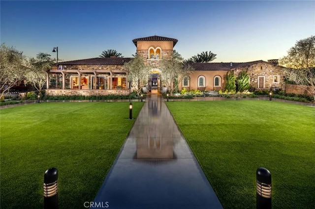 exterior space featuring a lawn, stone siding, a tiled roof, and stucco siding