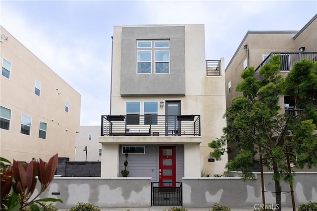 contemporary home with stucco siding, a balcony, and a fenced front yard
