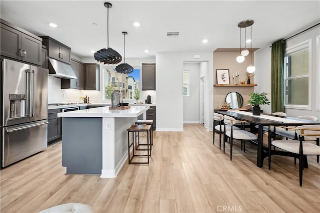 kitchen with light countertops, light wood finished floors, stainless steel appliances, a kitchen island, and under cabinet range hood