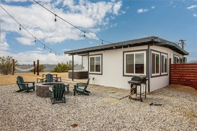 rear view of property featuring a jacuzzi, a patio, a fire pit, and fence