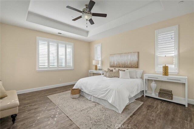 bedroom featuring baseboards, wood finished floors, and a tray ceiling