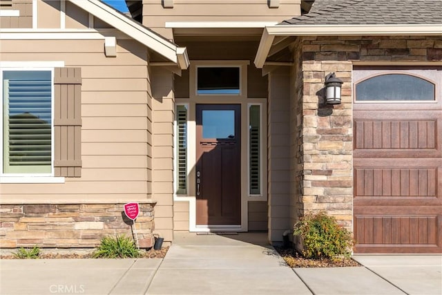 entrance to property with stone siding and a shingled roof