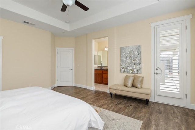 bedroom with wood finished floors, connected bathroom, a tray ceiling, baseboards, and visible vents