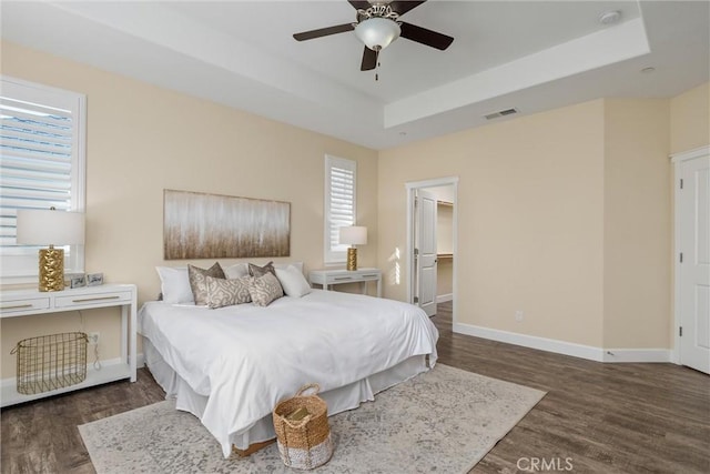 bedroom with visible vents, wood finished floors, a tray ceiling, and multiple windows