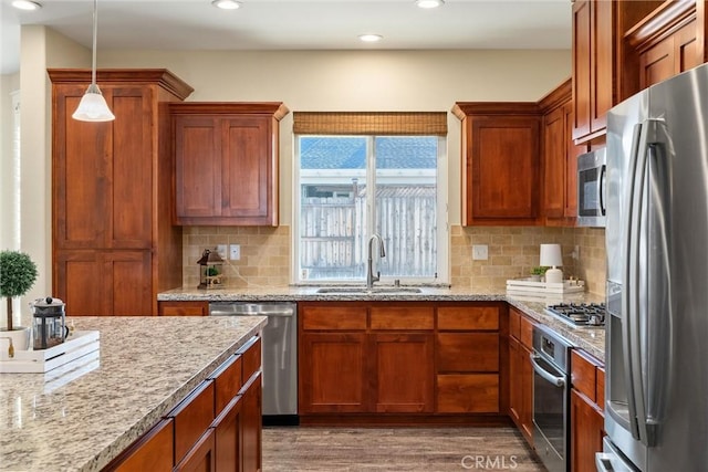 kitchen with wood finished floors, a sink, brown cabinetry, appliances with stainless steel finishes, and recessed lighting