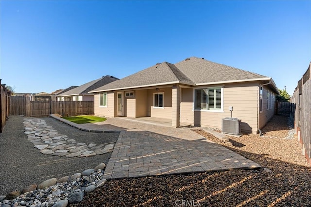 rear view of property featuring a fenced backyard, roof with shingles, central air condition unit, and a patio
