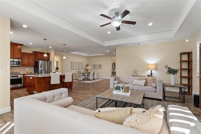living area featuring recessed lighting, a raised ceiling, dark wood-type flooring, and baseboards