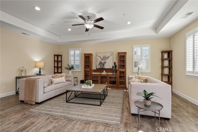 living room featuring a tray ceiling, wood finished floors, a ceiling fan, and plenty of natural light
