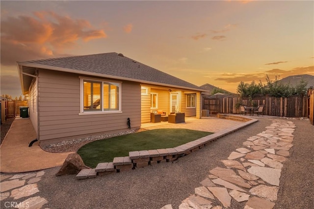 rear view of property with a fenced backyard, roof with shingles, outdoor lounge area, and a patio area