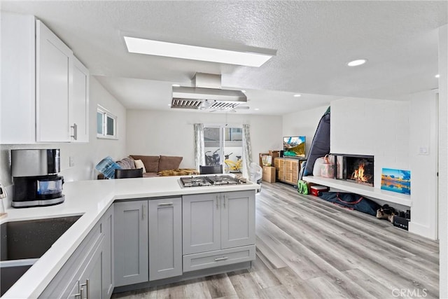 kitchen with a peninsula, gray cabinets, stainless steel gas stovetop, wall chimney range hood, and open floor plan