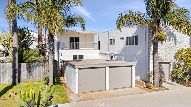 view of front of house with a balcony, fence, a garage, and stucco siding