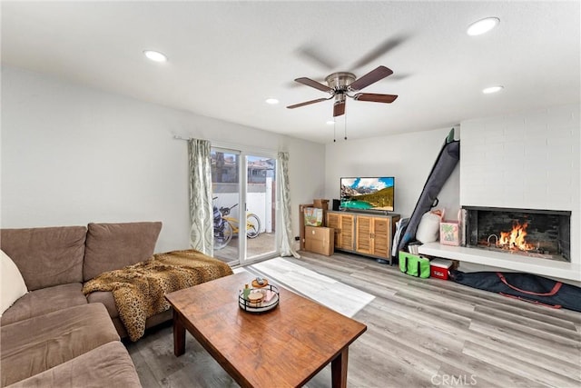 living room with a brick fireplace, light wood-style flooring, recessed lighting, and a ceiling fan