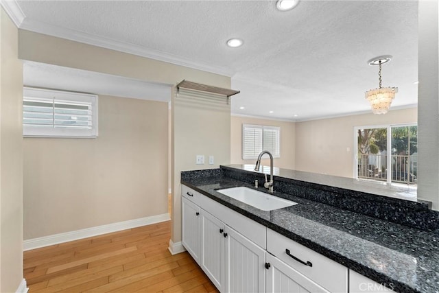 kitchen featuring a sink, dark stone counters, light wood-style floors, and ornamental molding