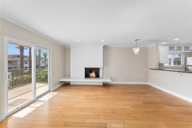 unfurnished living room with crown molding, baseboards, light wood-type flooring, a lit fireplace, and an inviting chandelier