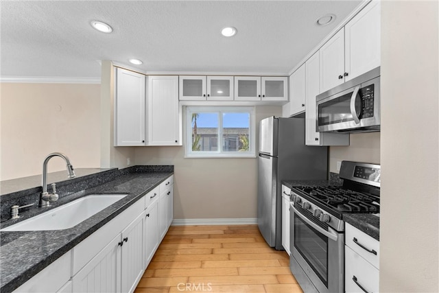 kitchen with a sink, light wood-style floors, appliances with stainless steel finishes, white cabinets, and glass insert cabinets