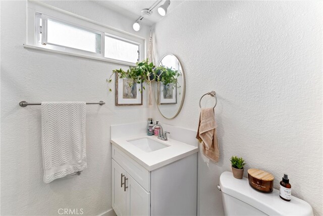 bathroom with toilet, vanity, and a textured wall