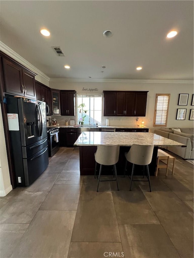 kitchen with black fridge with ice dispenser, dark brown cabinetry, stainless steel range with gas stovetop, visible vents, and ornamental molding