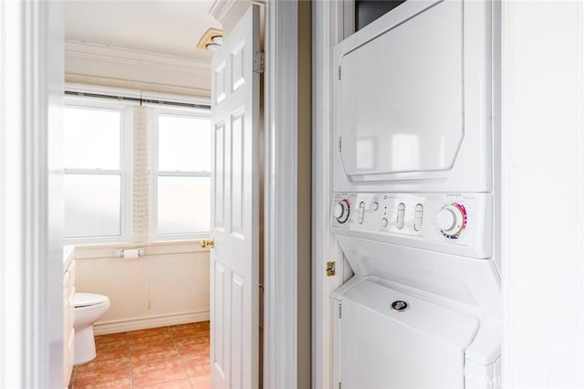 laundry room with stacked washer / dryer, laundry area, light tile patterned floors, baseboards, and ornamental molding