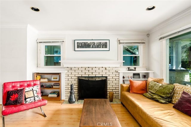 living area featuring recessed lighting, wood finished floors, ornamental molding, and a brick fireplace
