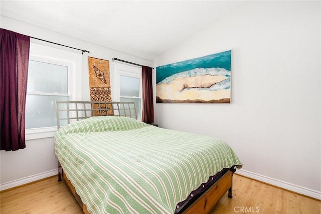 bedroom featuring baseboards, wood finished floors, and vaulted ceiling