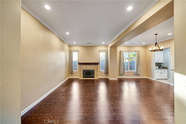 unfurnished living room featuring an inviting chandelier, recessed lighting, ornamental molding, a fireplace, and wood finished floors
