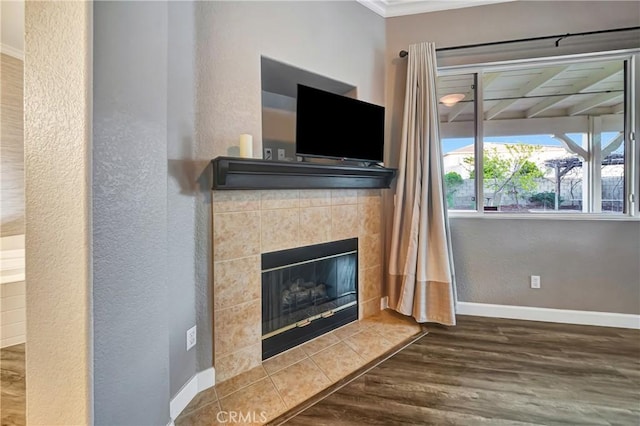 unfurnished living room featuring crown molding, a textured wall, a tiled fireplace, and wood finished floors