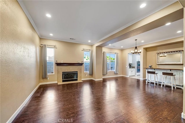 unfurnished living room featuring crown molding, a chandelier, baseboards, a glass covered fireplace, and wood finished floors