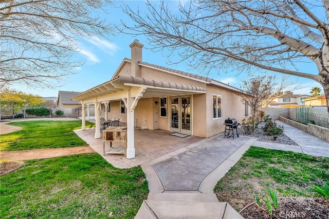back of house featuring a fenced backyard, a lawn, a chimney, stucco siding, and french doors
