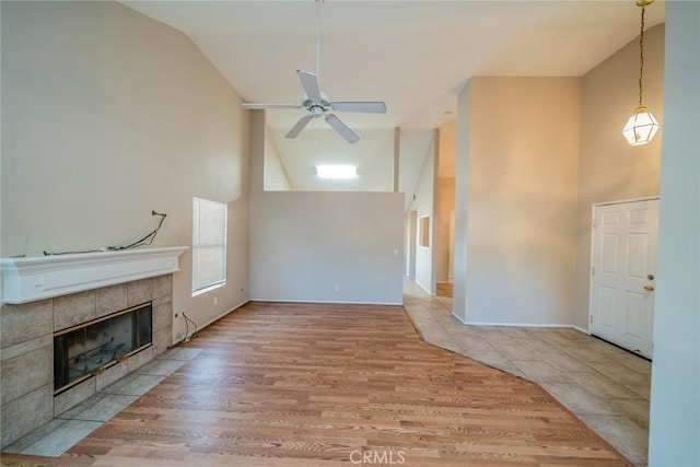 unfurnished living room with high vaulted ceiling, a tiled fireplace, a ceiling fan, and wood finished floors