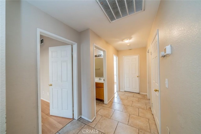 corridor featuring a sink, visible vents, baseboards, and light tile patterned floors