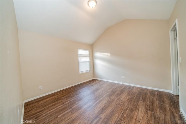 spare room featuring dark wood-style floors, baseboards, and lofted ceiling