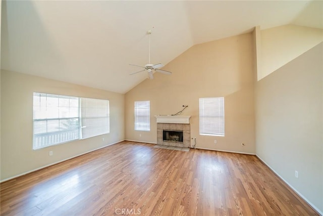 unfurnished living room with light wood-style floors, a tile fireplace, high vaulted ceiling, and a ceiling fan