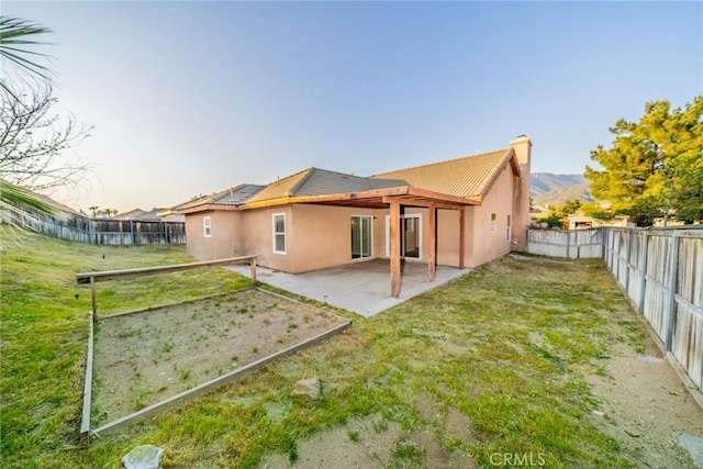 rear view of house featuring a yard, a fenced backyard, stucco siding, a patio, and a chimney