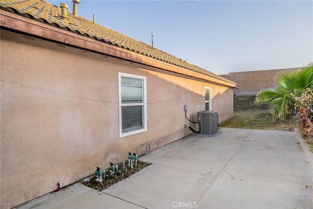 view of side of property with a patio area, stucco siding, and central AC