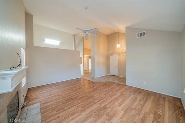 unfurnished living room featuring high vaulted ceiling, light wood-type flooring, a ceiling fan, visible vents, and a tiled fireplace