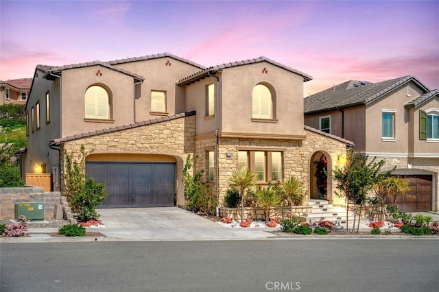 mediterranean / spanish house with concrete driveway, stucco siding, and stone siding