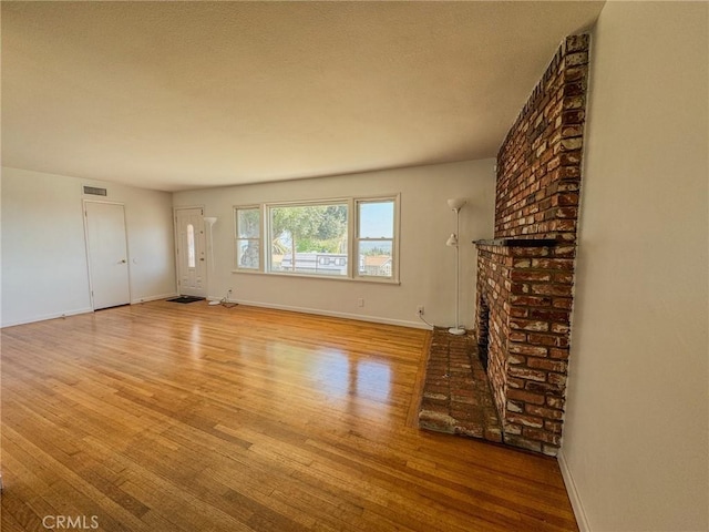 unfurnished living room featuring baseboards, visible vents, wood finished floors, and a brick fireplace
