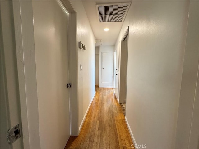 corridor featuring baseboards, visible vents, and light wood finished floors