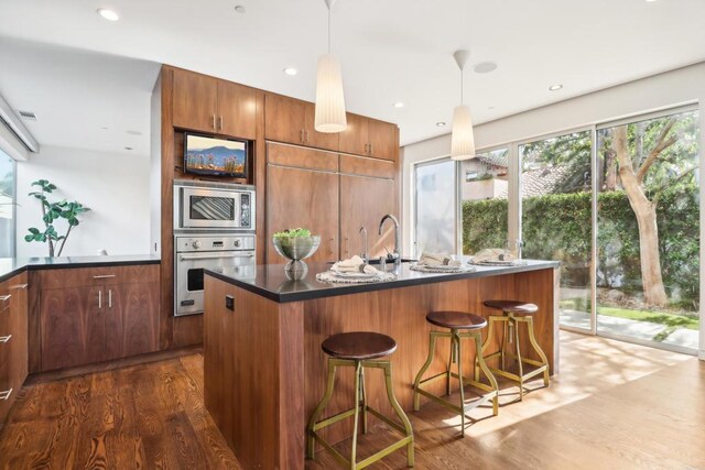 kitchen featuring pendant lighting, dark countertops, a sink, dark wood finished floors, and appliances with stainless steel finishes