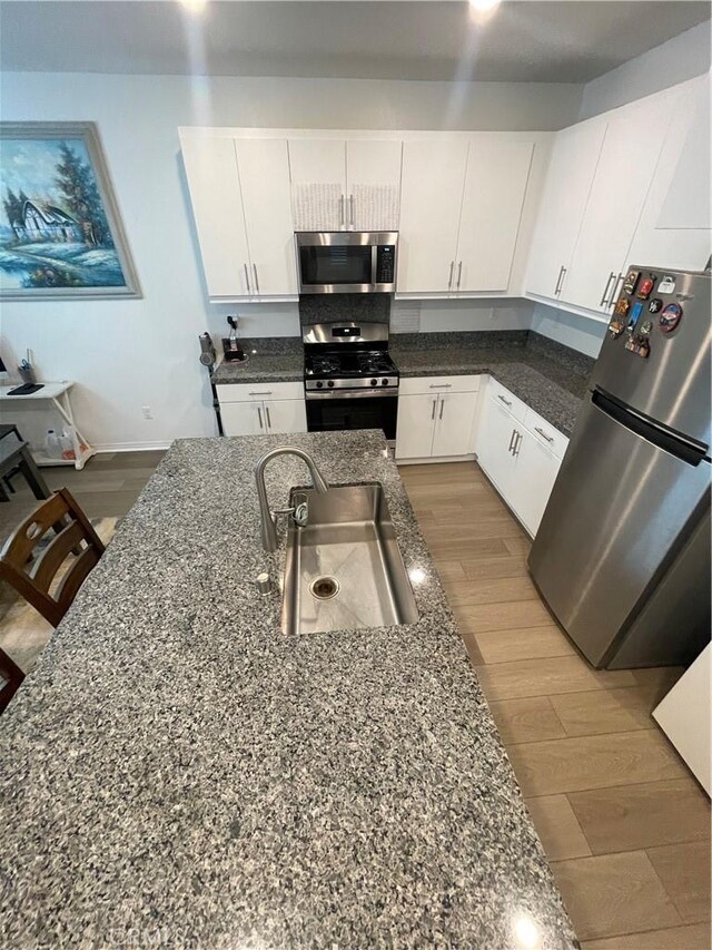 kitchen featuring stainless steel appliances, a sink, white cabinetry, wood finished floors, and dark stone countertops