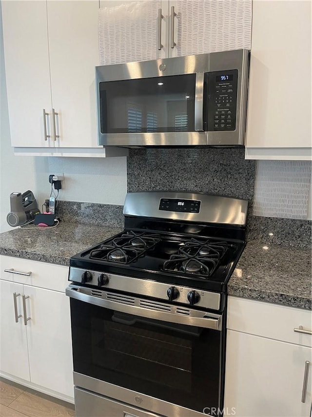 kitchen featuring stainless steel appliances, white cabinetry, decorative backsplash, and dark stone countertops