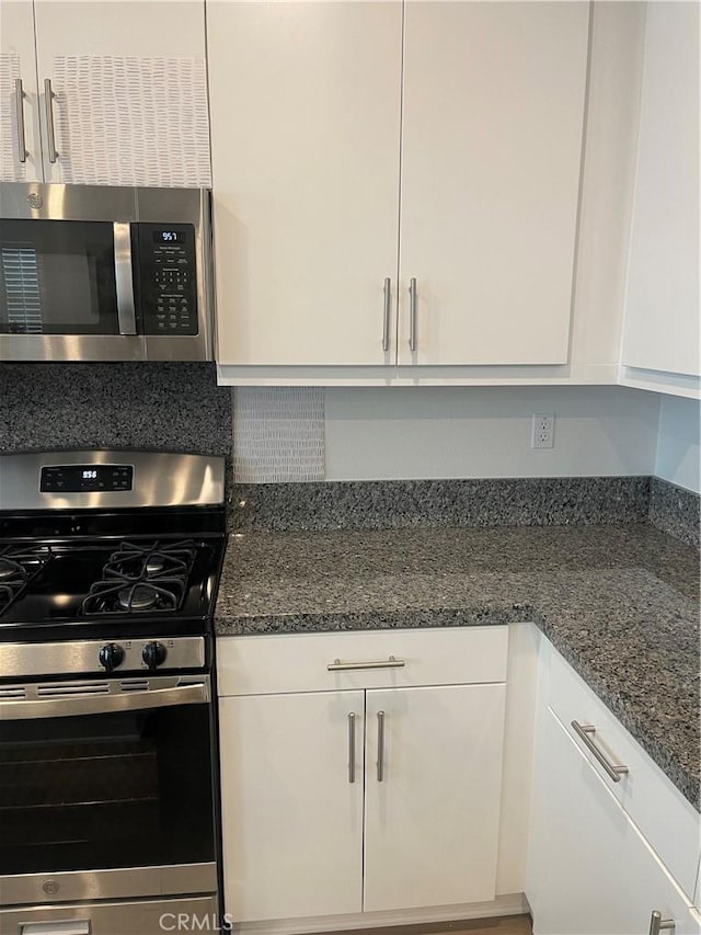 kitchen with appliances with stainless steel finishes, white cabinets, and dark stone counters
