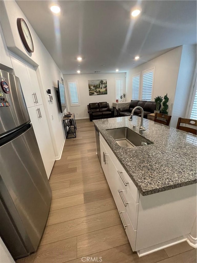 kitchen with freestanding refrigerator, a sink, a center island with sink, white cabinetry, and light wood-style floors