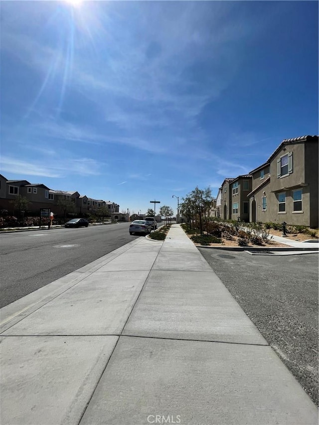 view of asphalt road with sidewalks, a residential view, street lights, and curbs